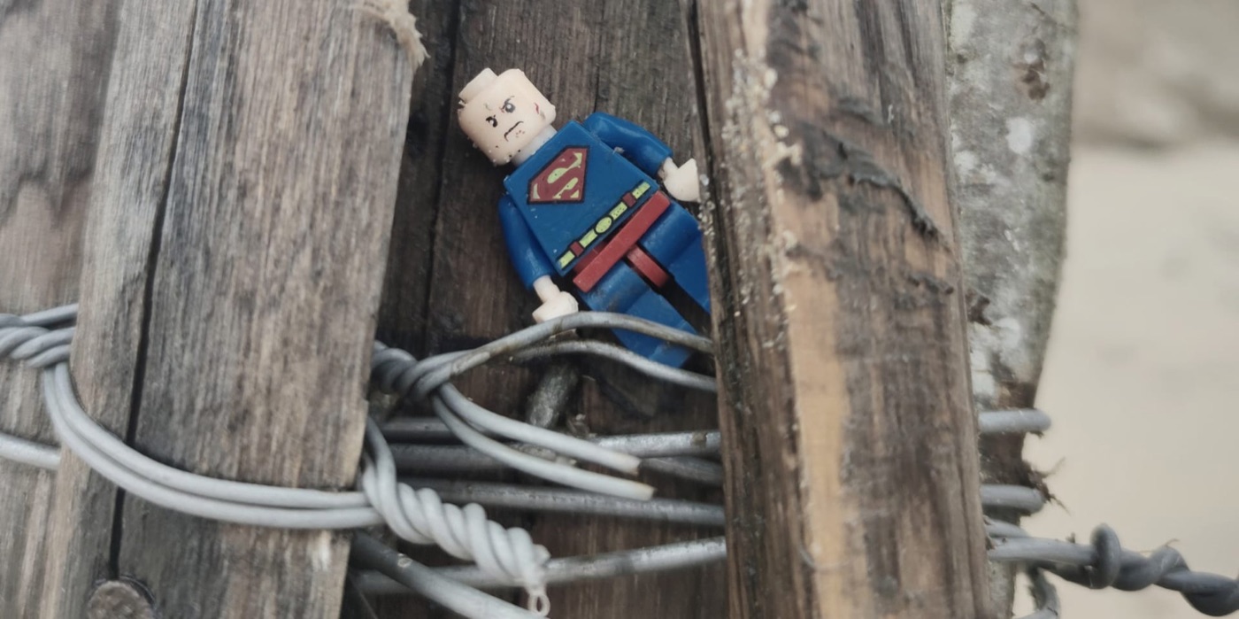 Un Superman Playmobil coincé entre deux piquets de clôture et des fils de fer